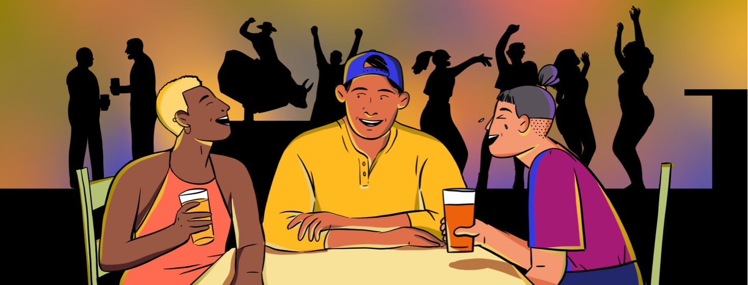alt=a man tells a funny story to people sitting at a table with him while people dance, drink, and ride a mechanical bull in the background.