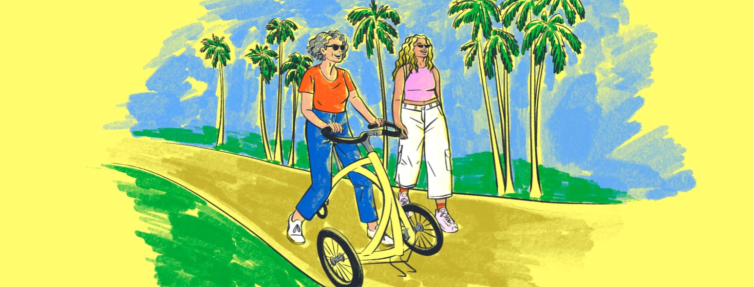 alt=a mother (using an assistive walker) and adult daughter walk down a path lined with palm trees